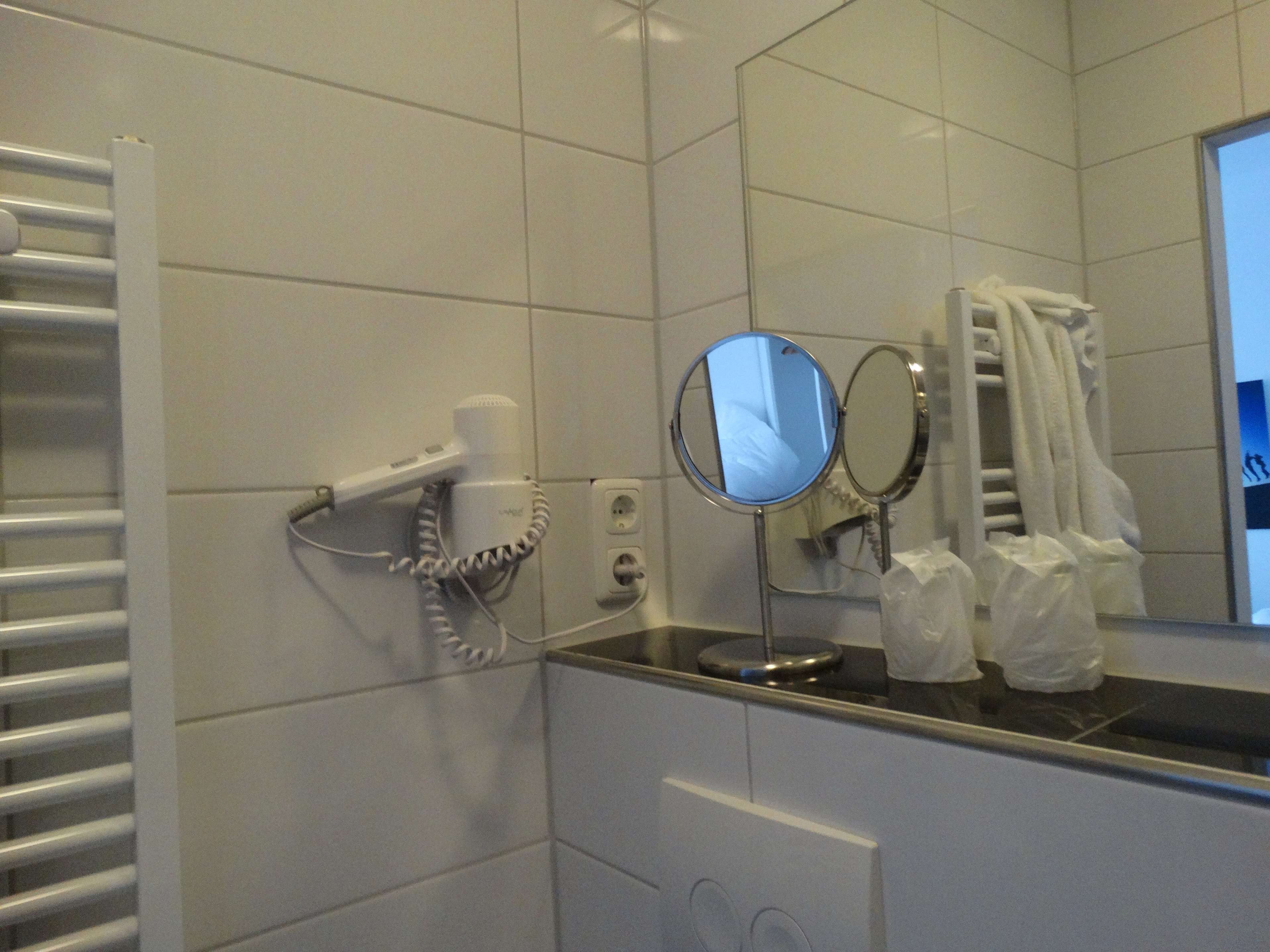 A bathroom with a towel rack, a hairdryer, a mirror, and a towel dispenser.