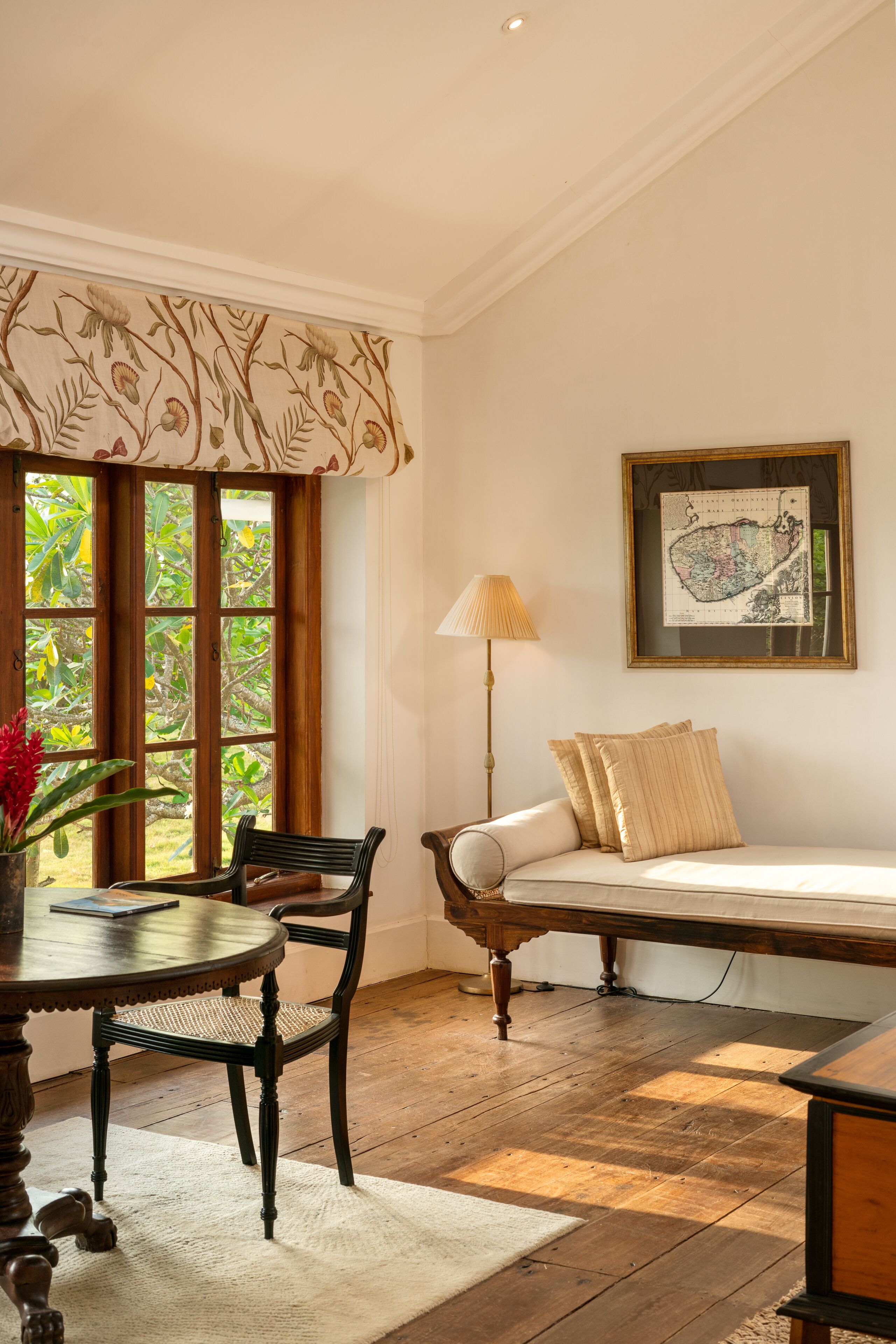 Una habitación con piso de madera, una mesa de comedor con sillas, un sofá con cojines, una lámpara y un mapa enmarcado en la pared.