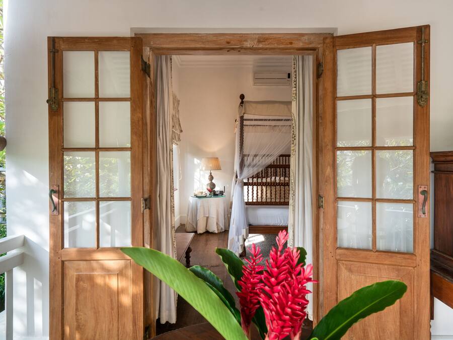A wooden door with glass panels leading to a room with a bed and a table with a lamp.