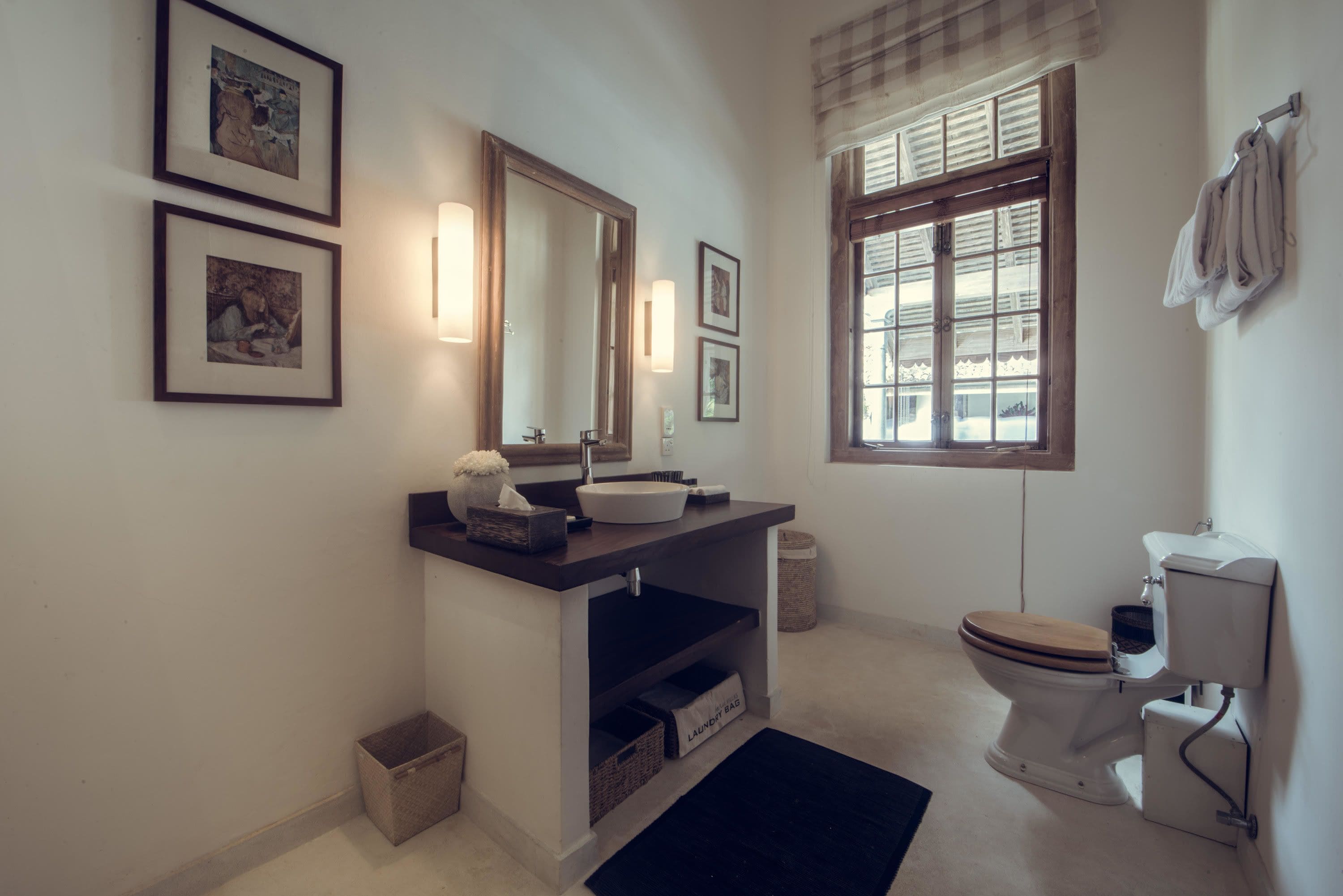 A bathroom with a sink, mirror, toilet, and framed pictures on the wall.
