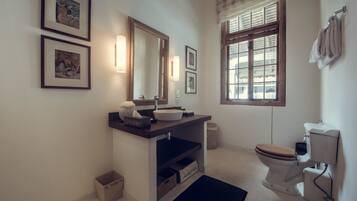 A bathroom with a sink, mirror, toilet, and framed pictures on the wall.
