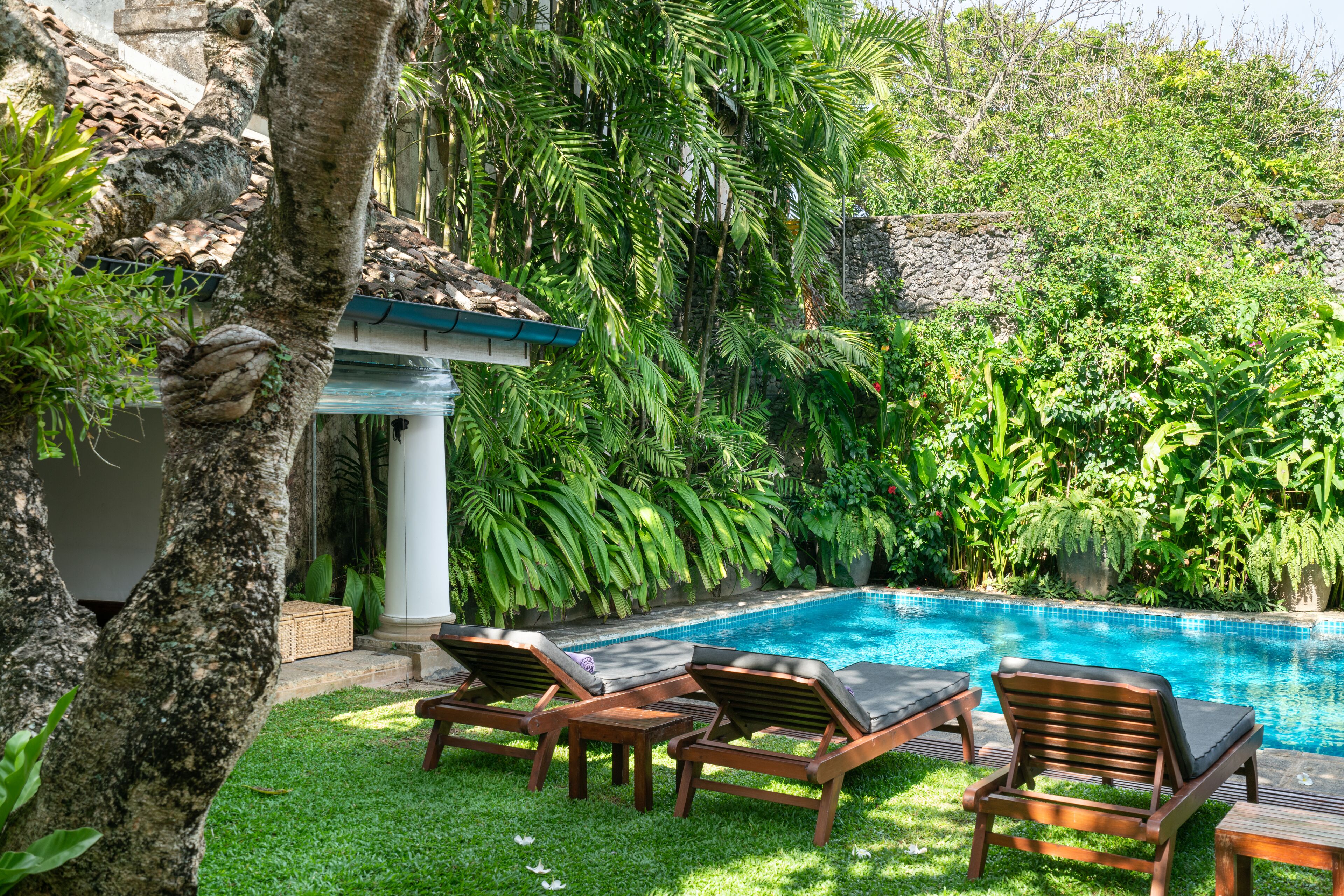 Un área junto a la piscina con sillones de descanso y un muro de piedra.