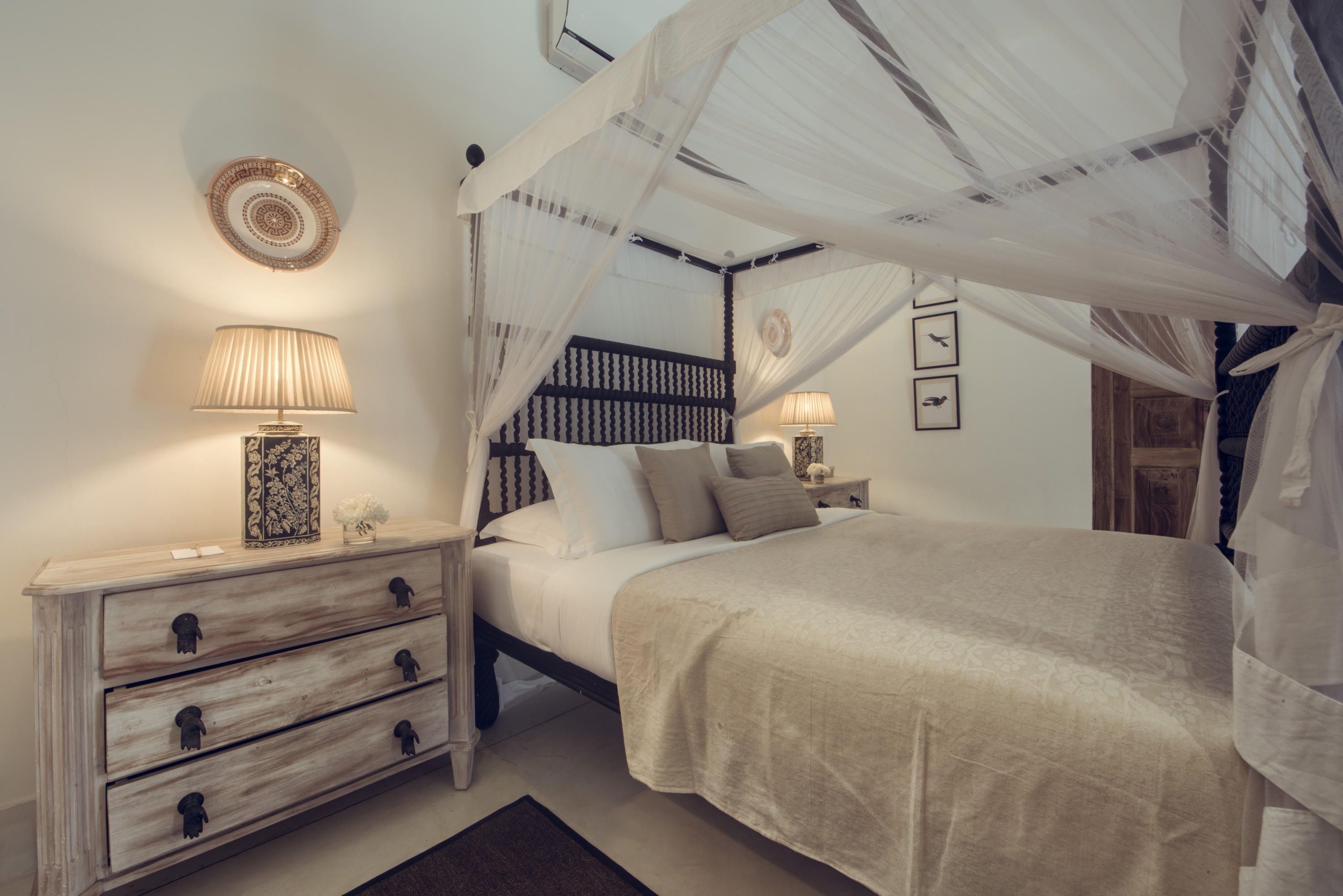A bedroom with a canopy bed, bedside tables with lamps, and a decorative wall plate.