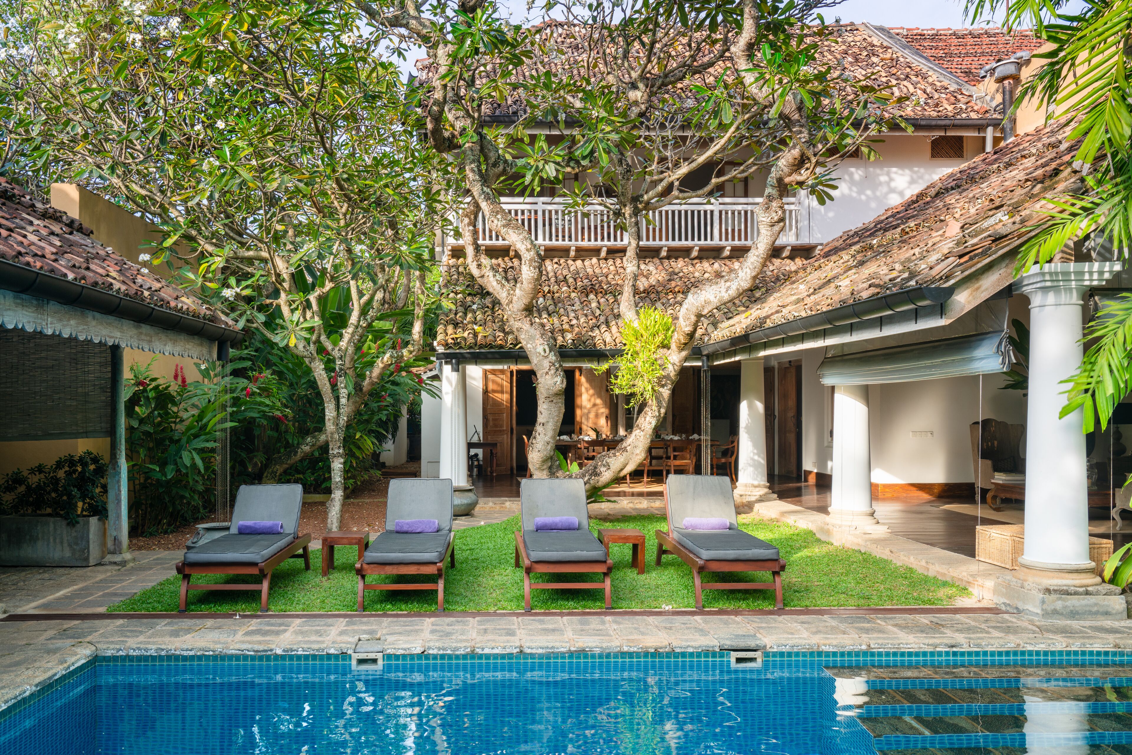 A poolside area with lounge chairs, a tree, and a building with a tiled roof.