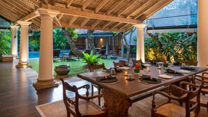 Un espace de restauration en plein air avec une table en bois prévue pour quatre personnes, entourée de chaises, et surplombé d’une pergola en bois dotée de colonnes.