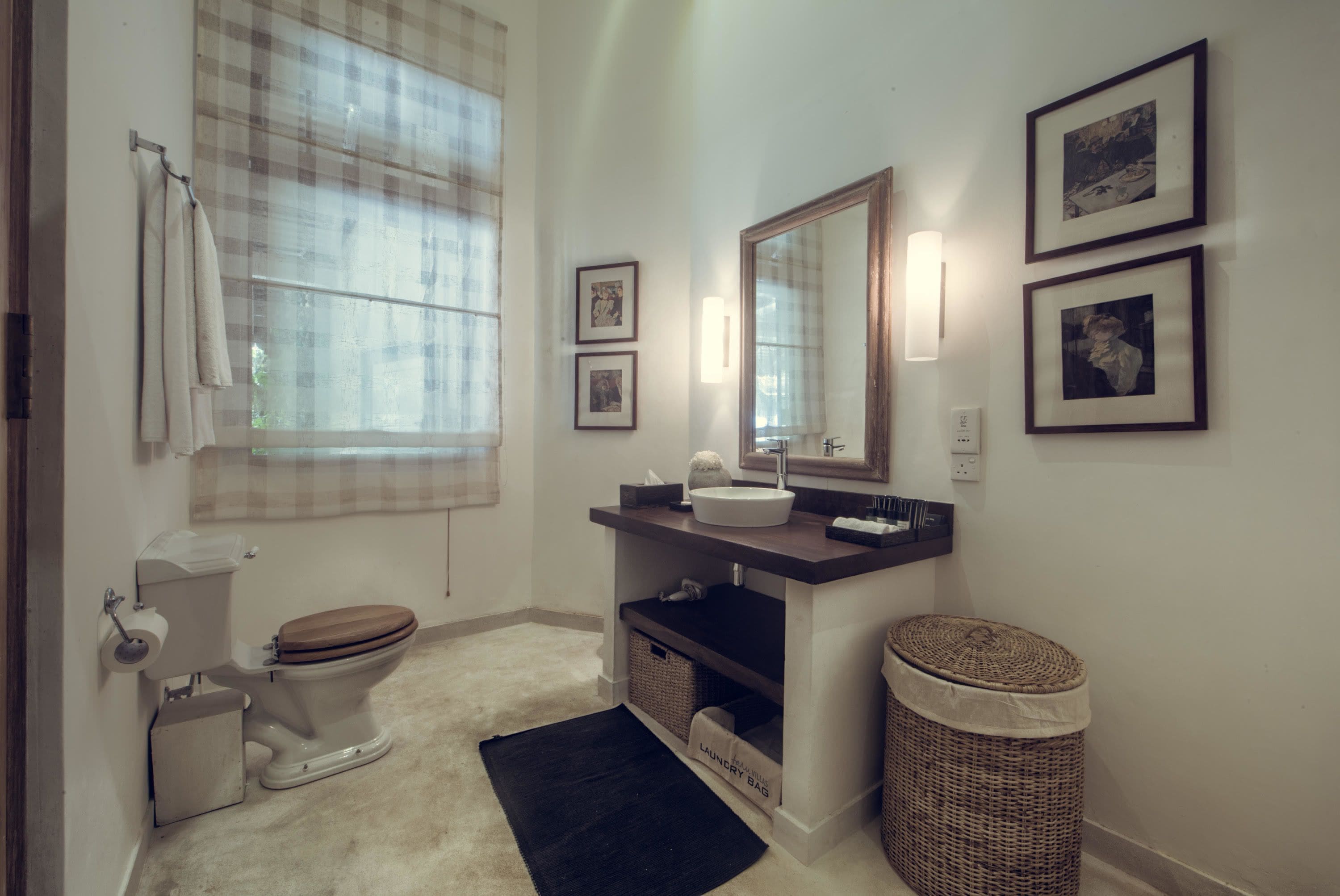A bathroom with a toilet, sink, mirror, and framed pictures on the wall.