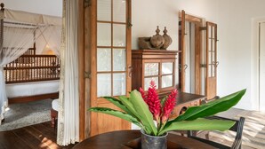 Une pièce avec un lit en bois, une table à manger ornée d’un vase de fleurs et un buffet en bois.
