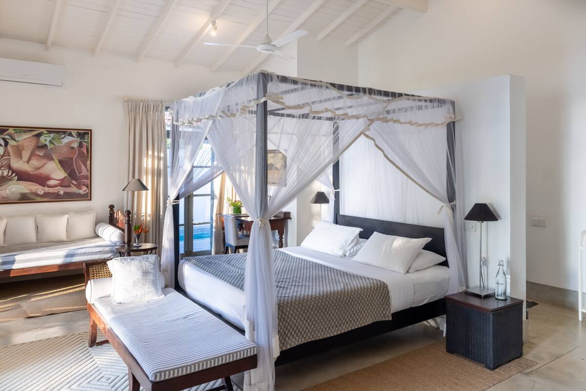 Une chambre spacieuse dotée d’un lit à baldaquin, d’un canapé et offrant une vue sur la mer.