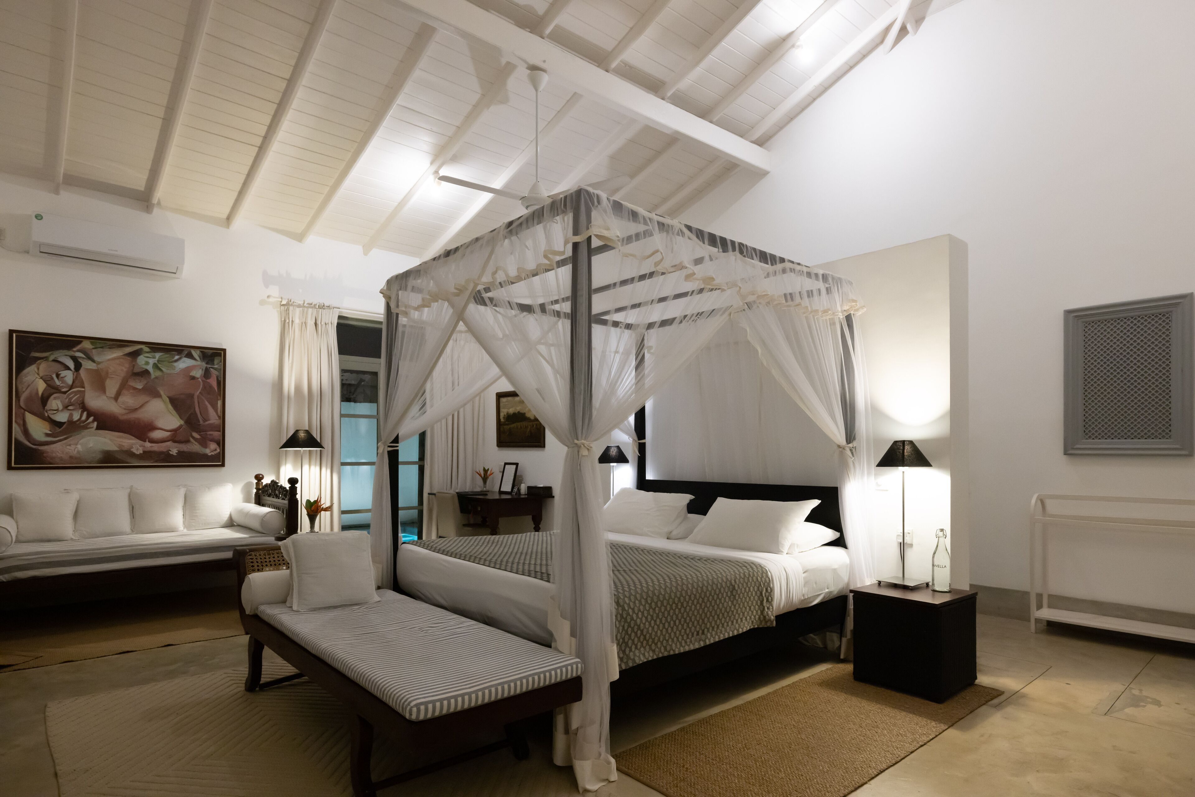 Ein Schlafzimmer mit Himmelbett, Tagesbett, Nachttisch und Lampe.