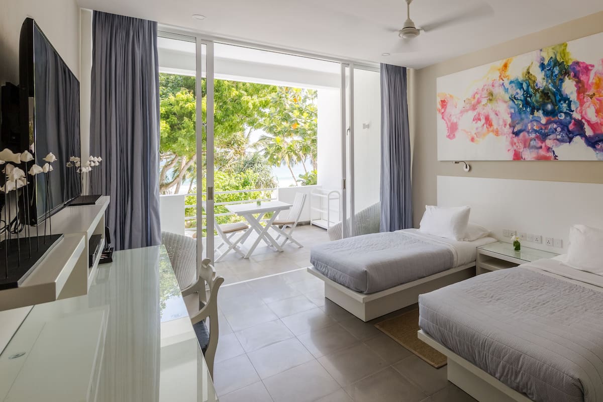 Une chambre d’hôtel avec deux lits, un bureau, une télévision et un balcon donnant sur un espace verdoyant.