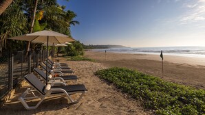 Un espace de détente au bord de la plage, avec des chaises longues et des parasols, une plage de sable et une vue sur l’océan.