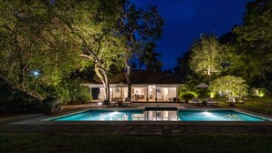 Un espace aménagé au bord de la piscine, comprenant une maison, du mobilier d’extérieur et des arbres.