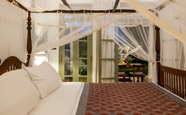 Une chambre à coucher avec un lit à baldaquin, une vue sur le jardin et un coin repas éclairé à l’extérieur.