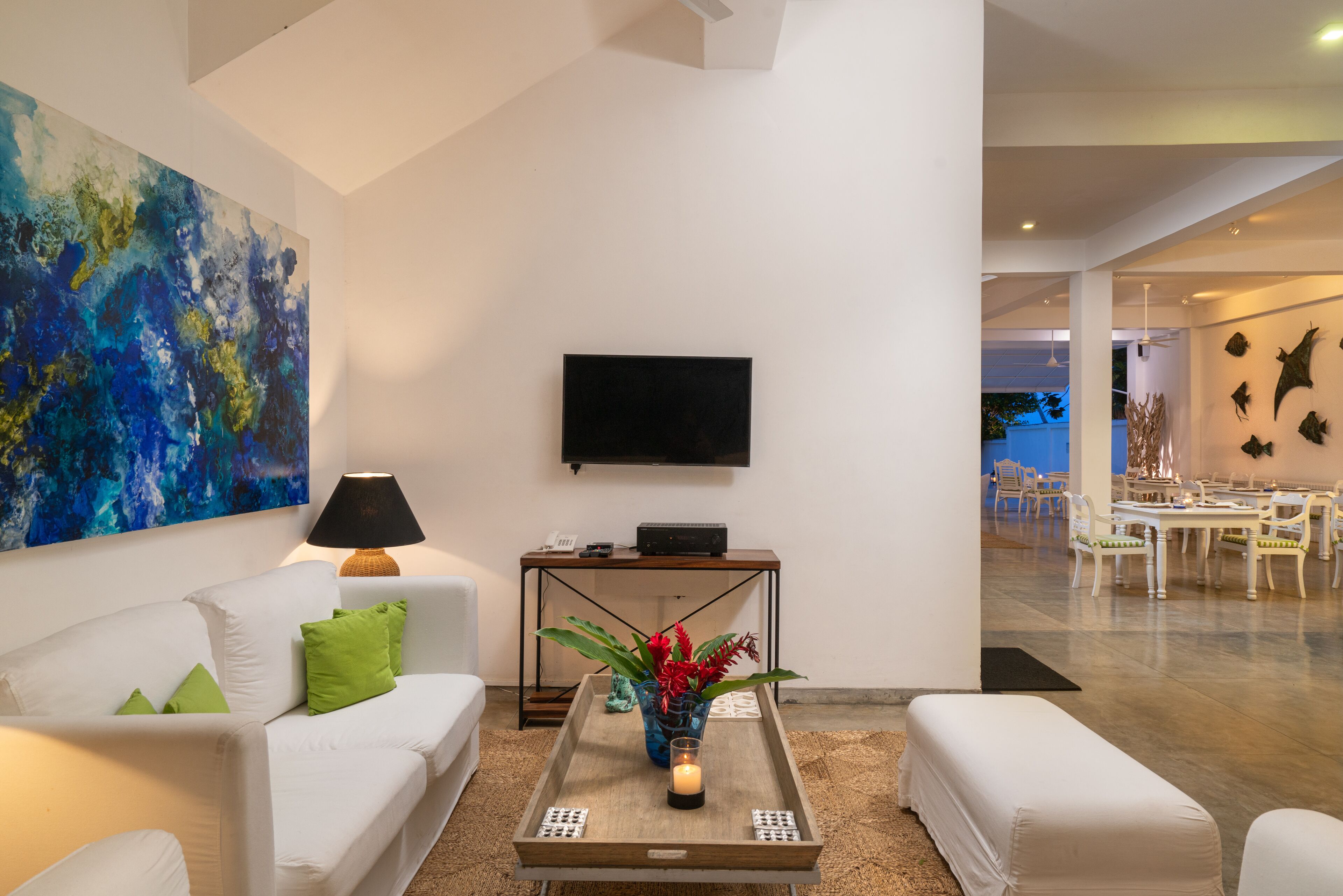 A modern living room with a white sofa, green cushions, a coffee table with a candle, and a large abstract painting.