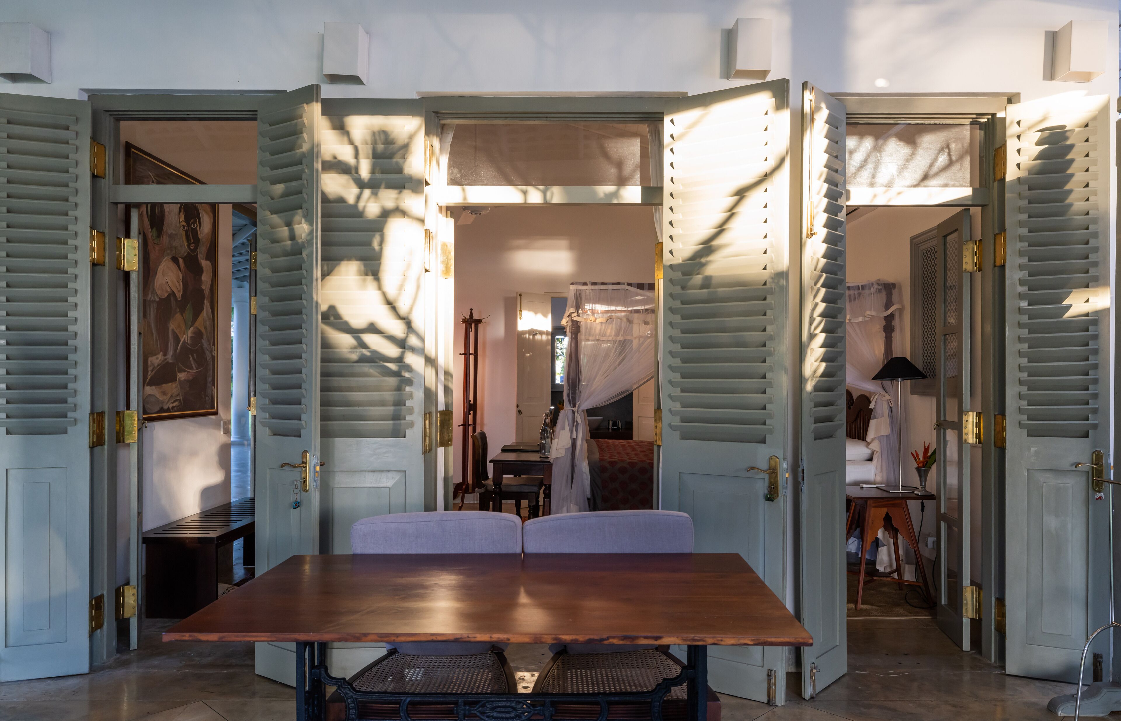 A room with a wooden table and chairs, a bed with a white canopy, and a window with blinds.