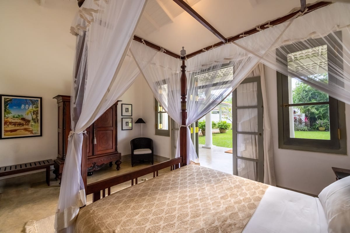 Une chambre à coucher avec un lit à baldaquin, un banc, une chaise et une grande fenêtre donnant sur un paysage verdoyant.