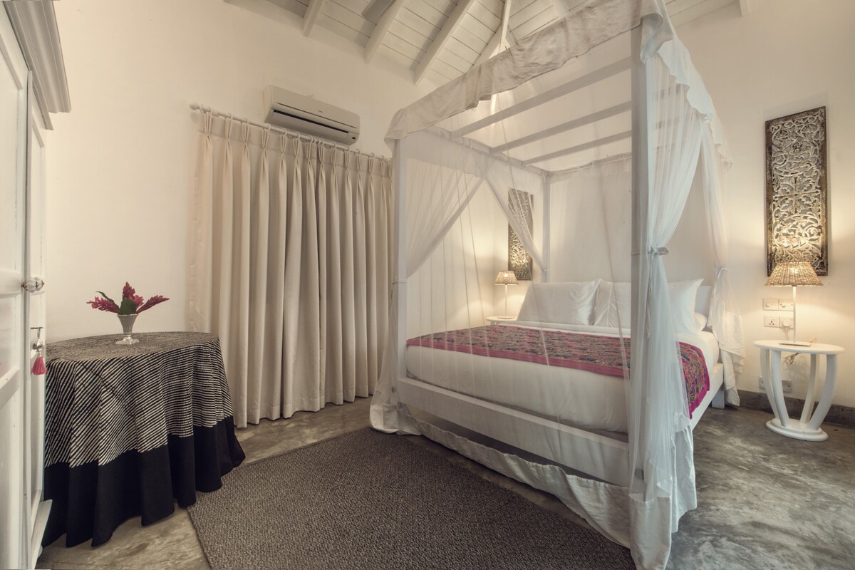 A bedroom with a four-poster bed, a bedside table, a lamp, and a curtain.