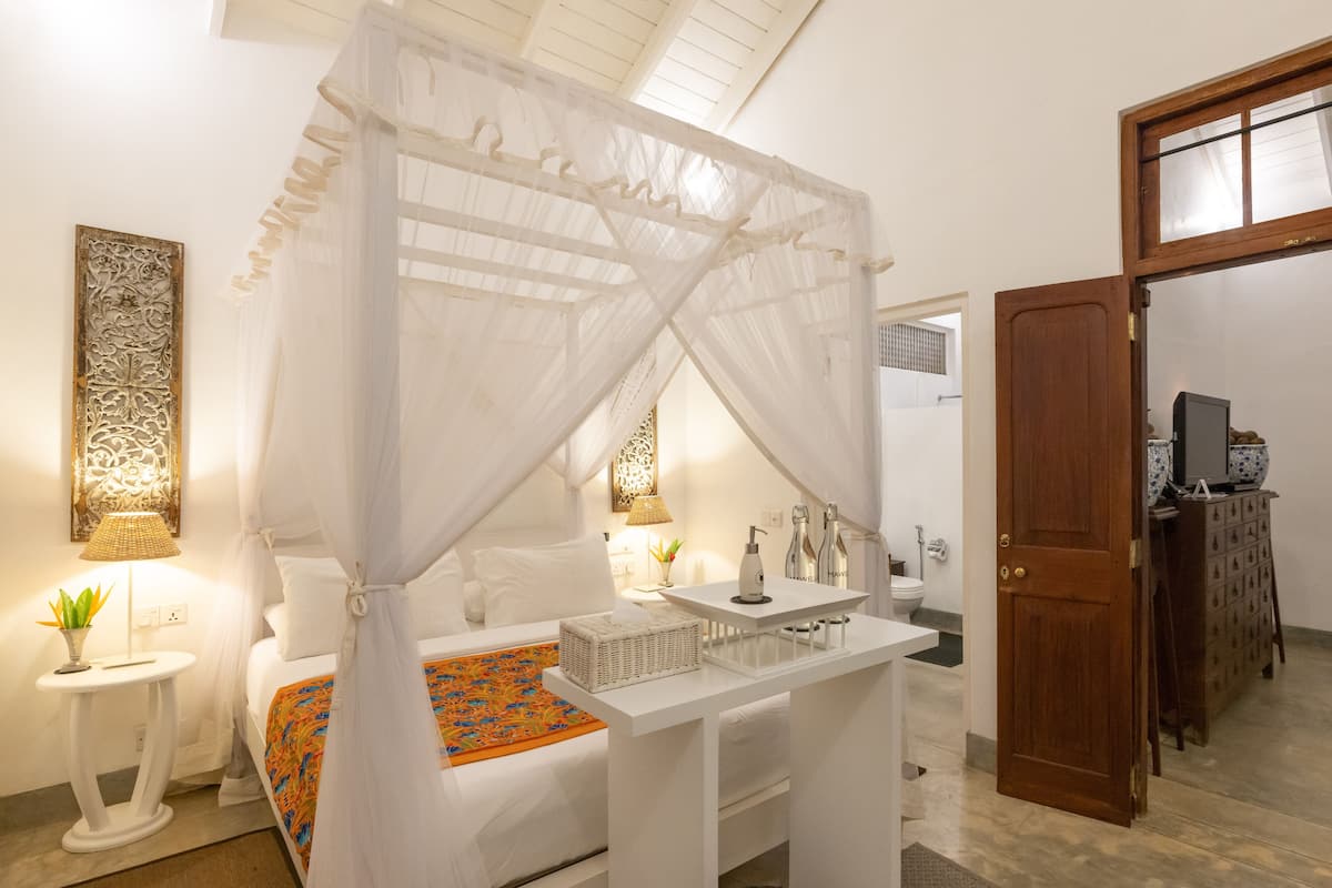 Une chambre à coucher avec un lit à baldaquin, une table de chevet, une lampe, un élément décoratif mural et une vue sur la salle de bain.