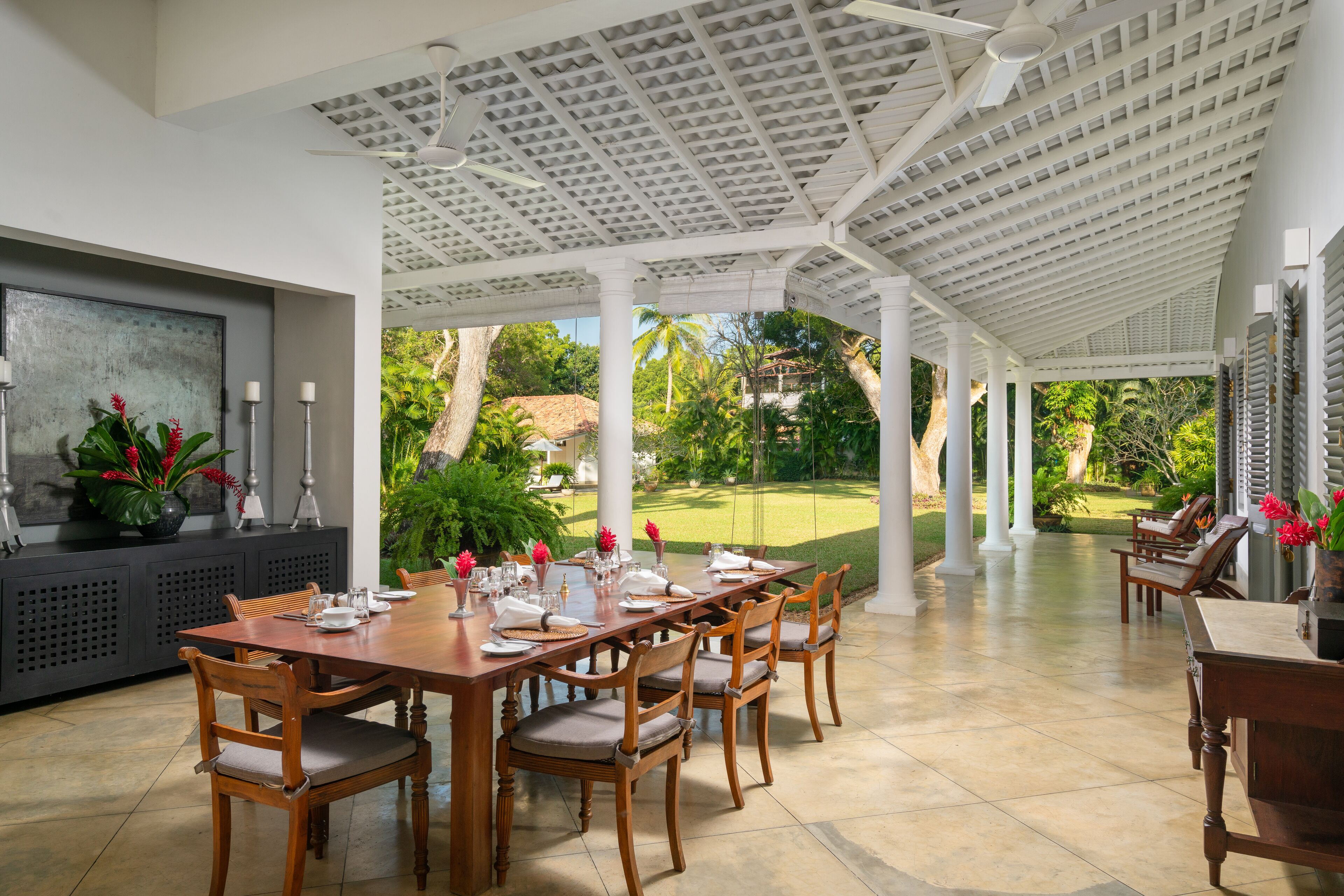 A covered outdoor dining area with a long wooden table set for six, surrounded by chairs.