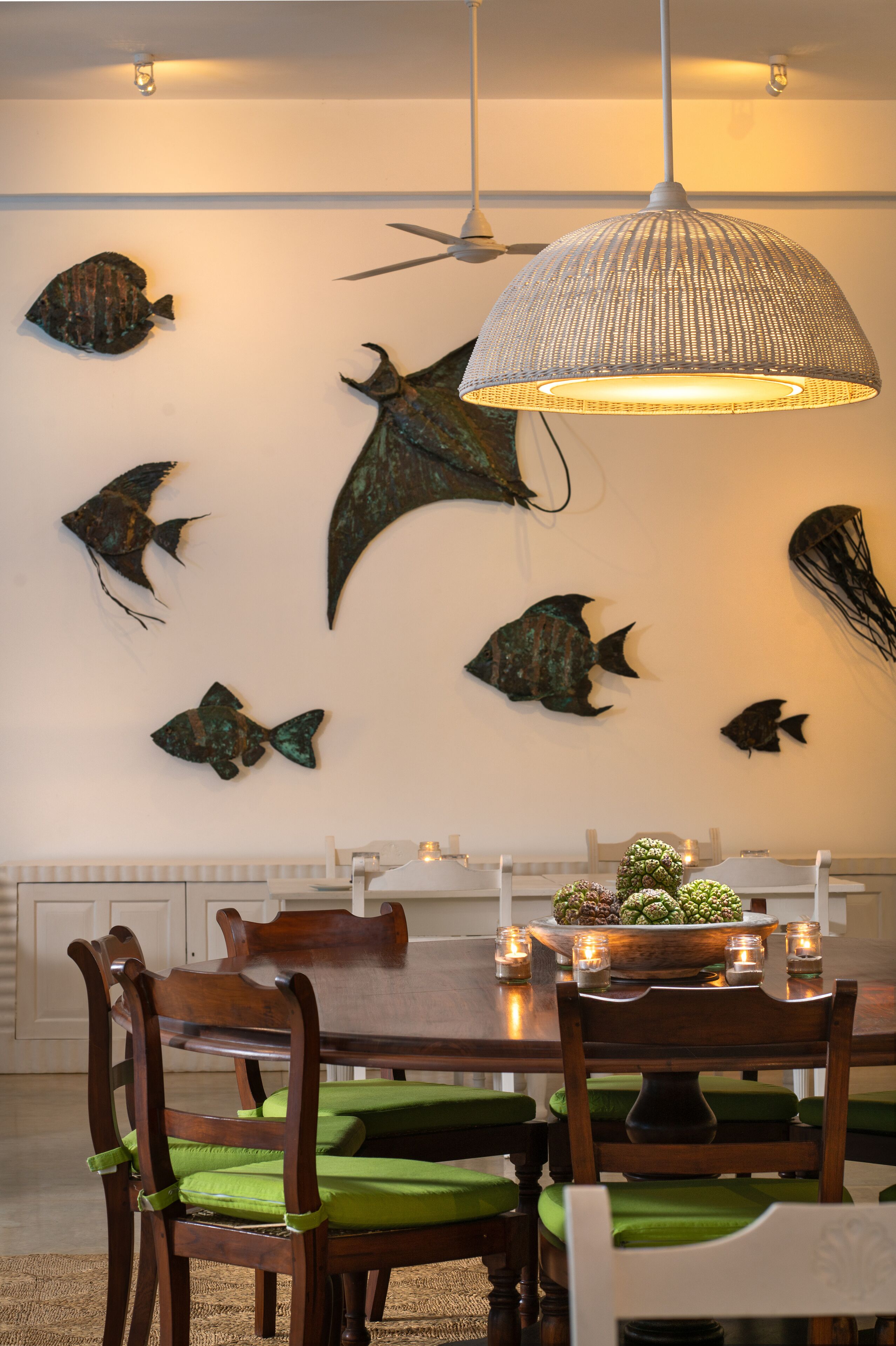 A dining area with a wooden table, green cushioned chairs, and a hanging light fixture.