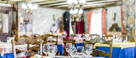 A dining area with tables set for service, featuring chandeliers and a stone wall in the background.