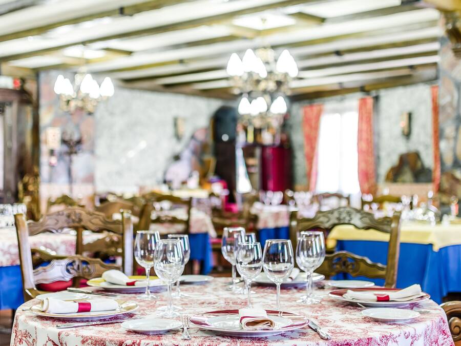 A dining area with tables set for service, featuring chandeliers and a stone wall in the background.