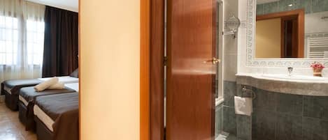 Habitación de hotel con dos camas, ducha, baño con un espejo grande y ventana con cortinas.
