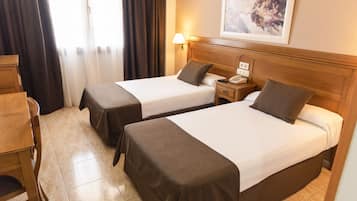 Habitación de hotel con dos camas, una mesita de noche de madera con teléfono, una lámpara y un cuadro en la pared.
