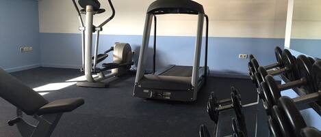 Un gimnasio con equipo de ejercicio, incluyendo cinta de correr, elíptica y banco de pesas.