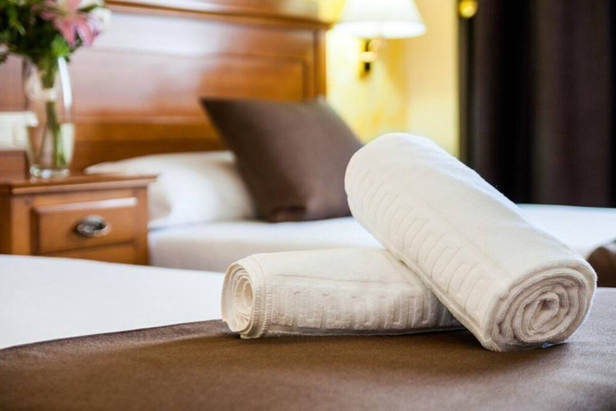 A neatly made bed with a rolled white towel and a brown pillow in a hotel room.