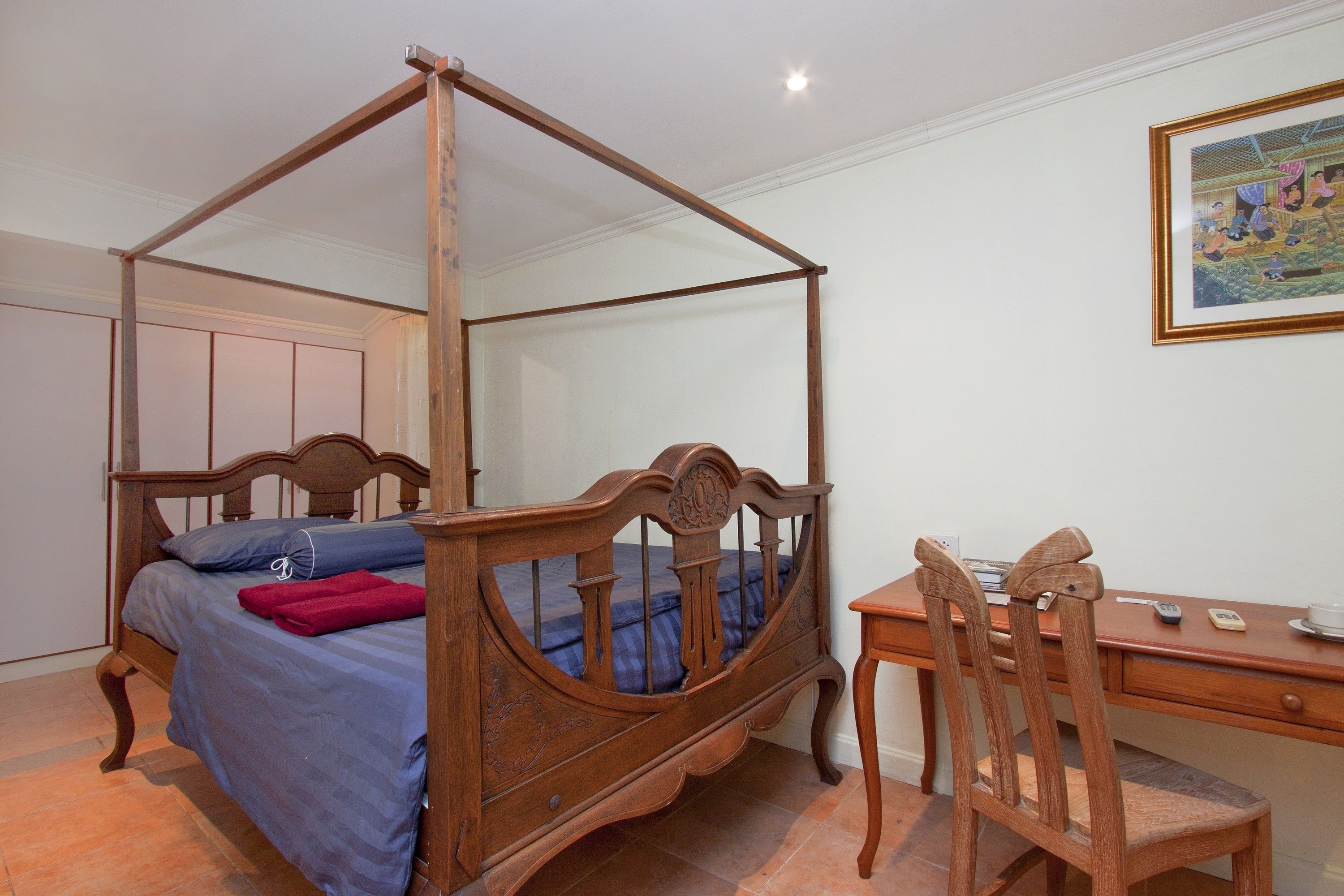 A bedroom with a four-poster bed, a wooden desk, and a chair.