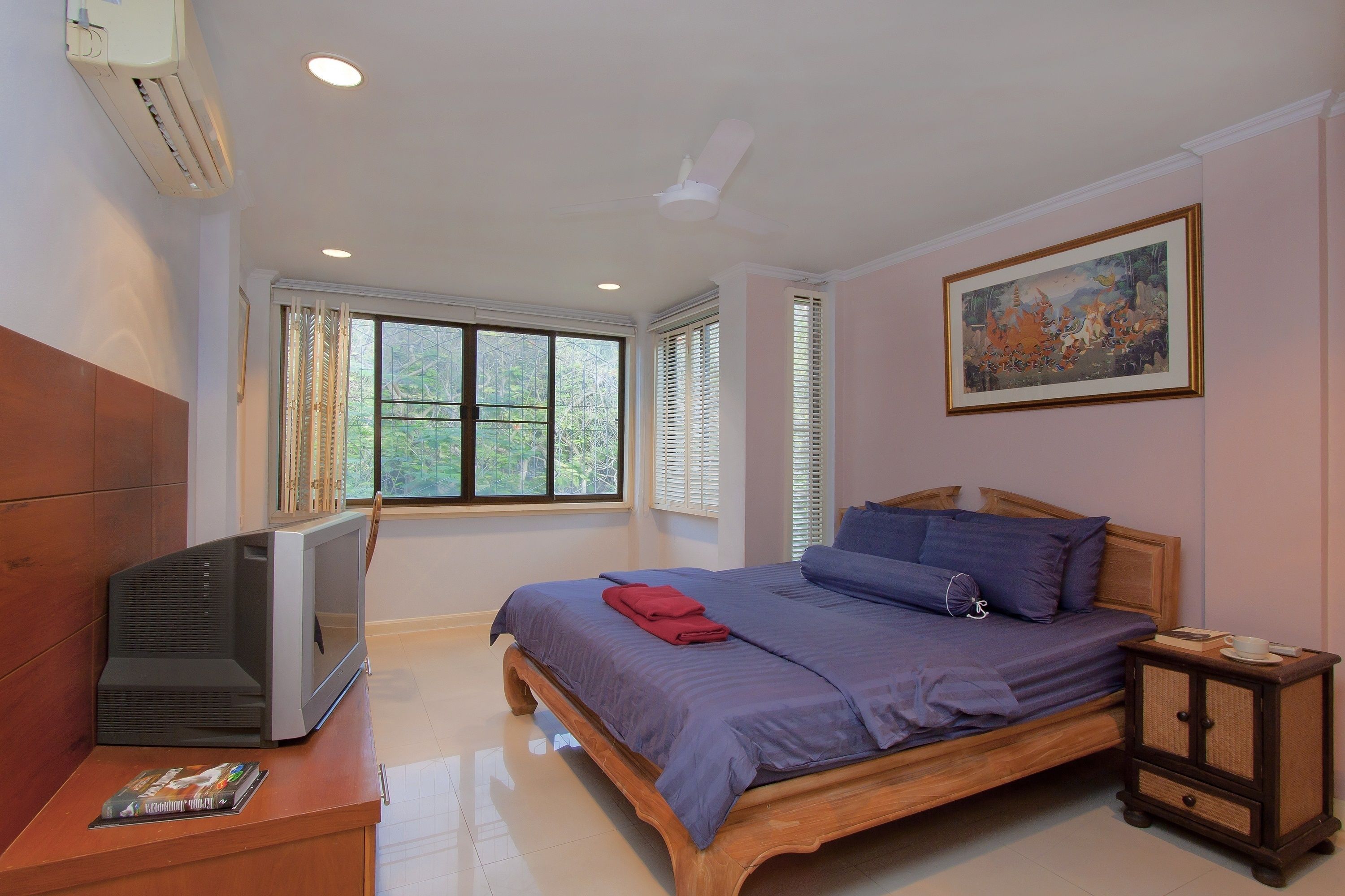A bedroom with a bed, a TV, a nightstand, and a window with blinds.