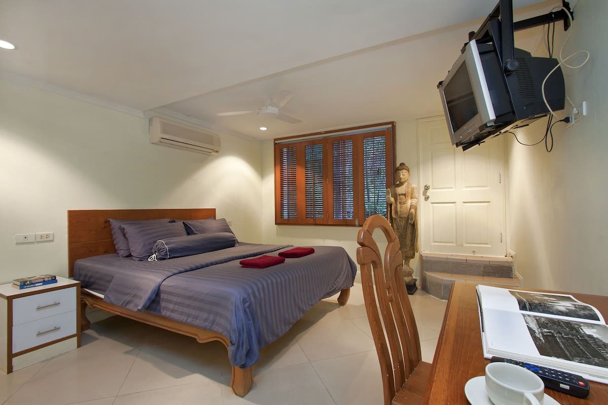 Een slaapkamer met een bed, nachtkastje en een aan de muur bevestigde televisie.