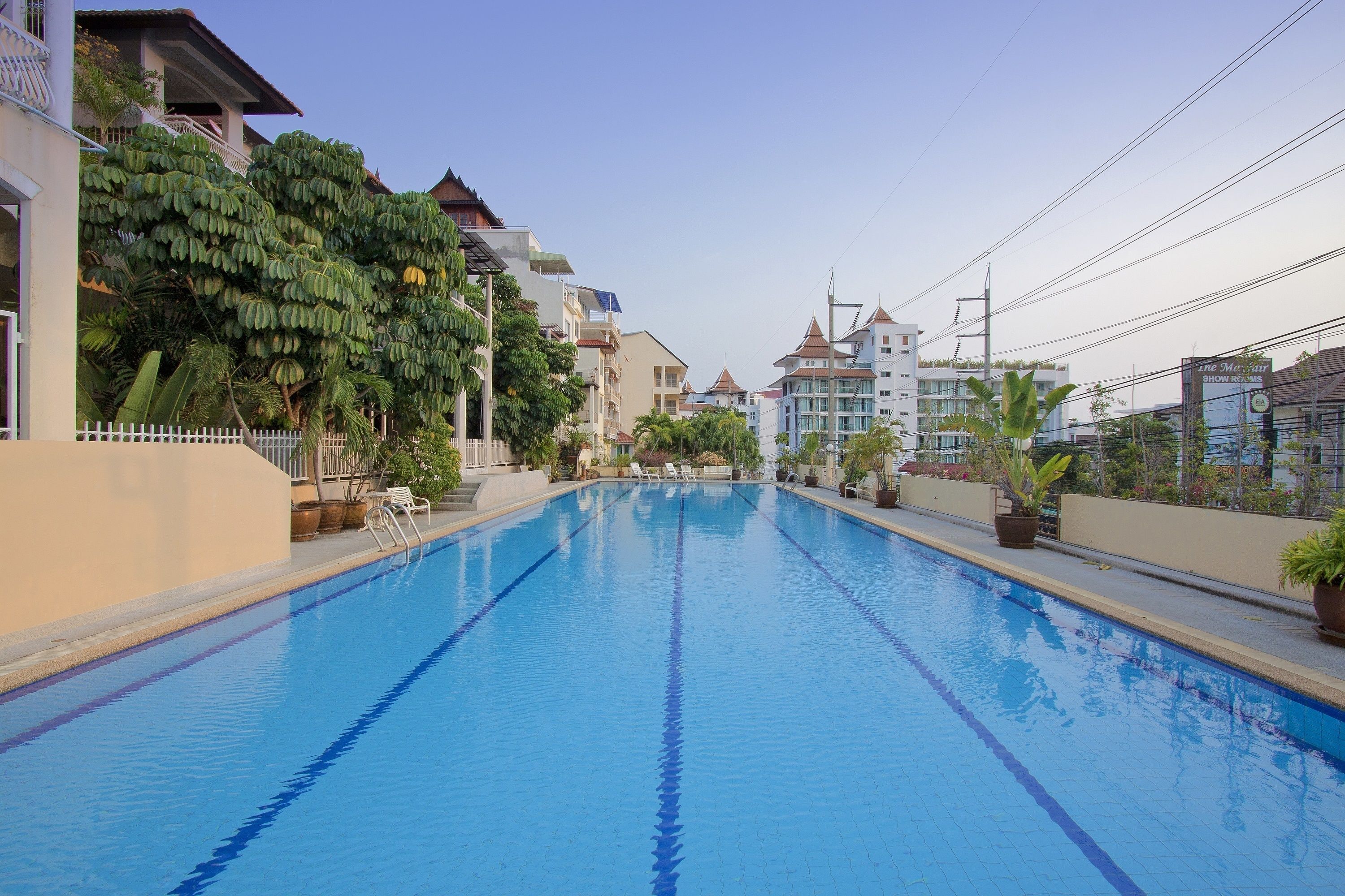 A swimming pool with clear blue water, surrounded by buildings and potted plants.