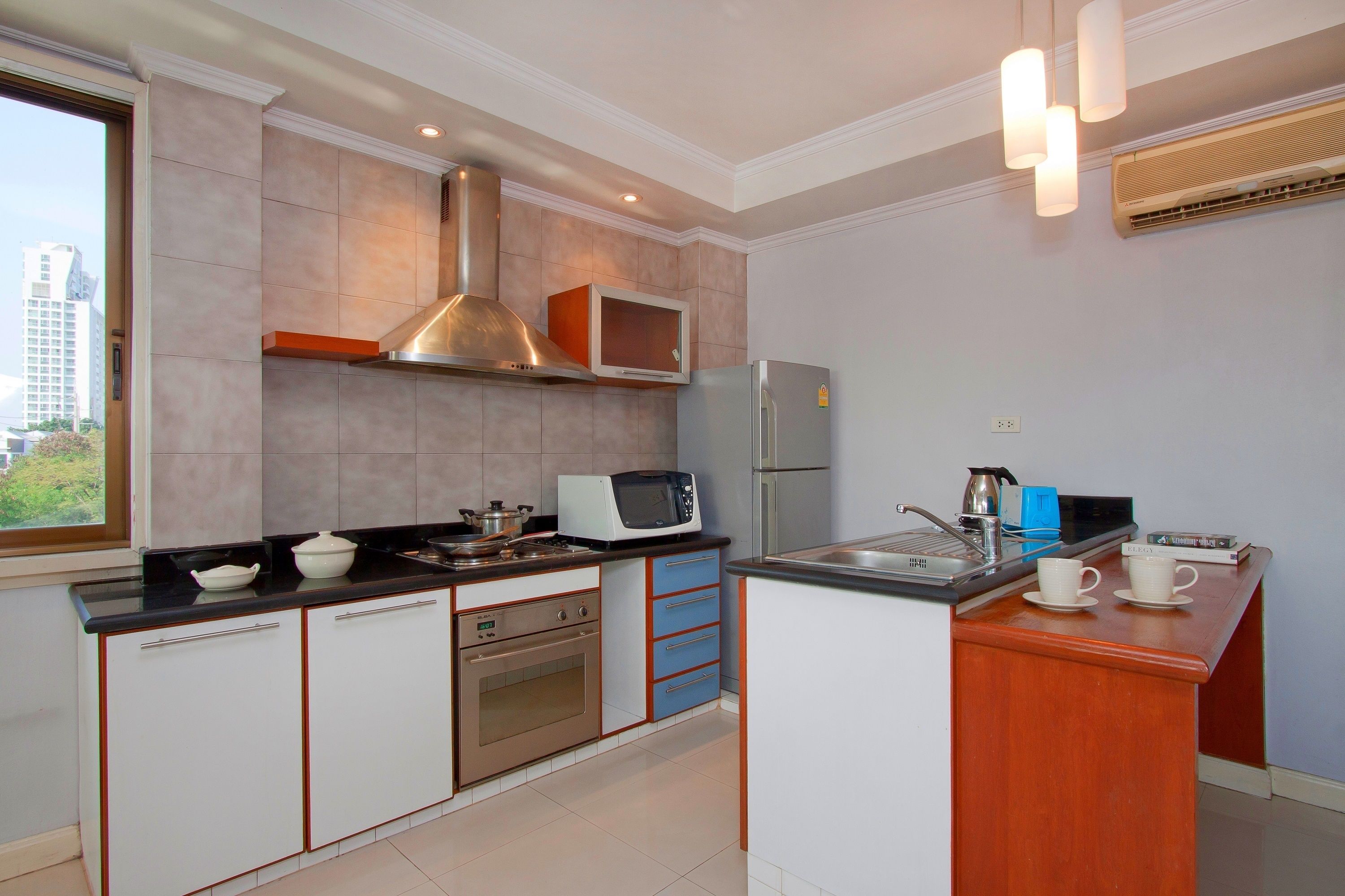 A modern kitchen with a built-in oven, microwave, and refrigerator. There is a window providing a view of the cityscape.