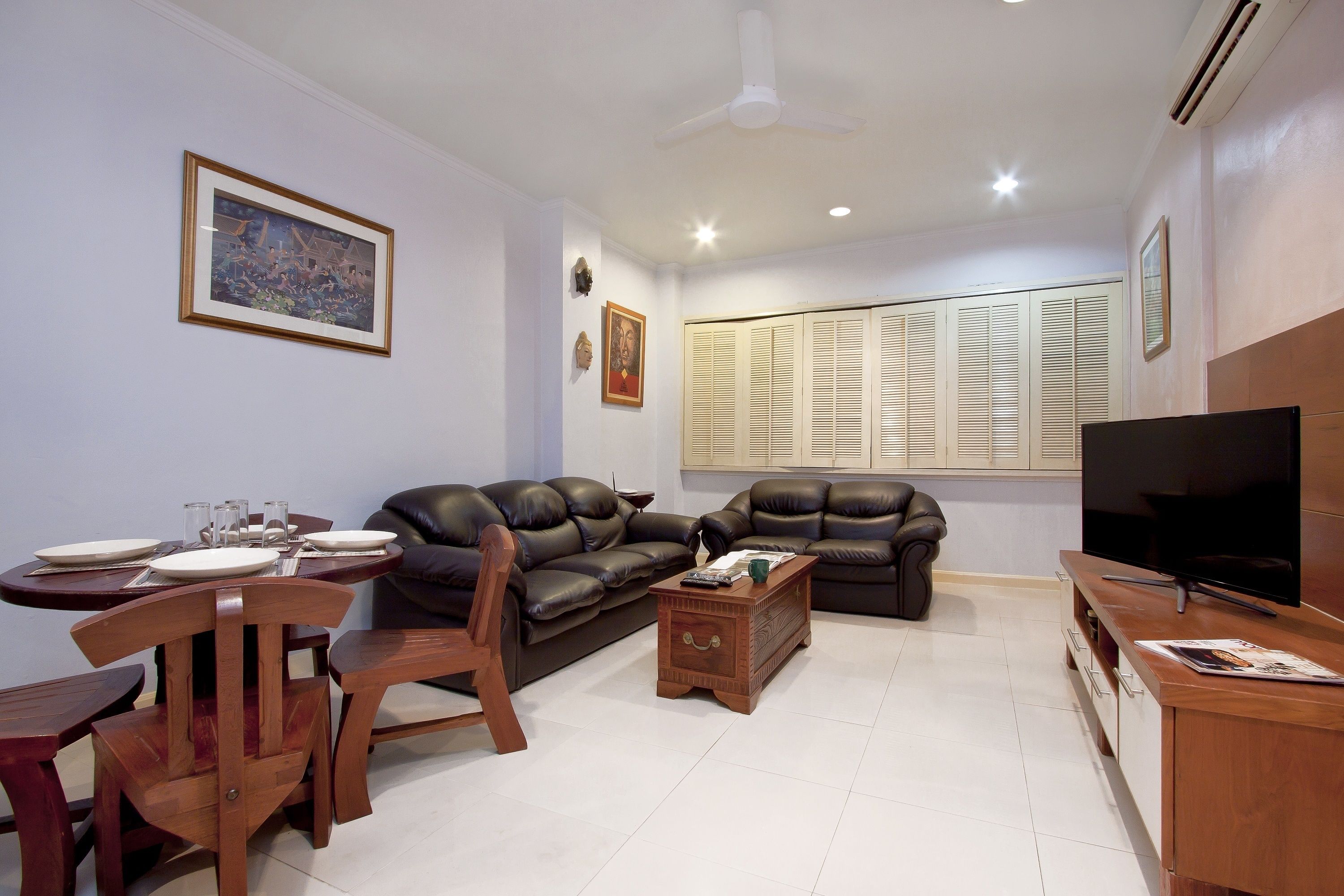 A living room with a dining table, two sofas, a coffee table, a TV, and a ceiling fan.