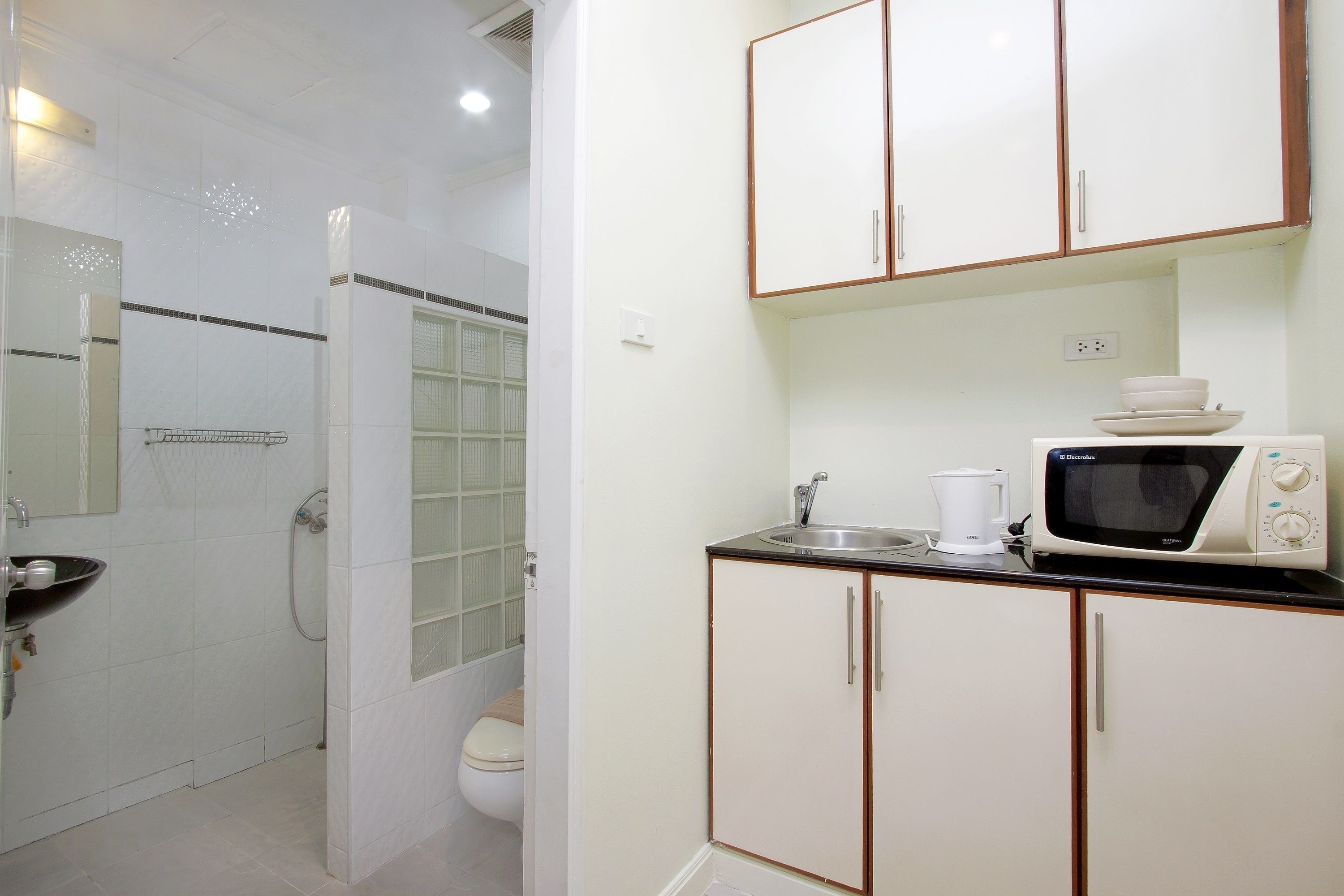 A bathroom with a toilet, shower, and sink. There is a microwave and a coffee maker on the counter.
