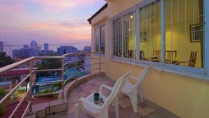Een balkon met uitzicht op de stad bij zonsondergang, met een hek, een stoel en een tafel met een mok.