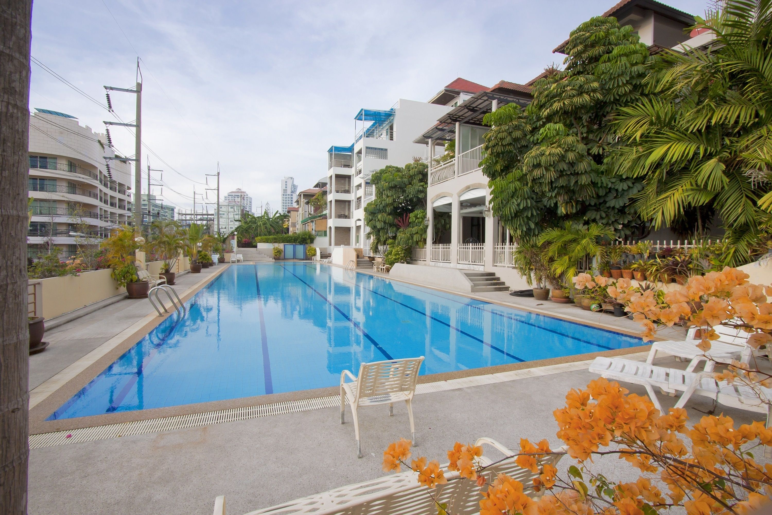 A swimming pool with lounge chairs and potted plants, surrounded by buildings and greenery.