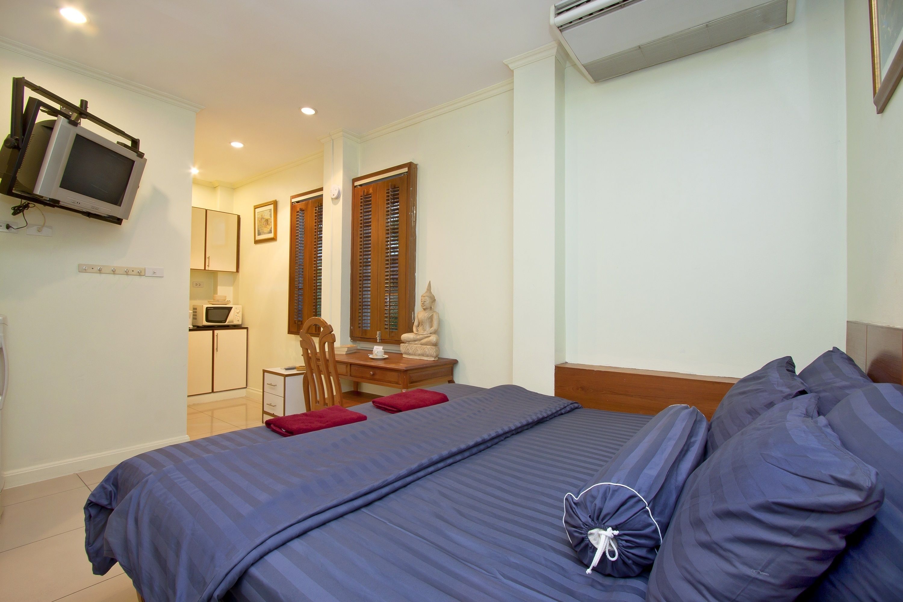 A bedroom with a bed, a desk, a chair, a television, and an air conditioning unit.