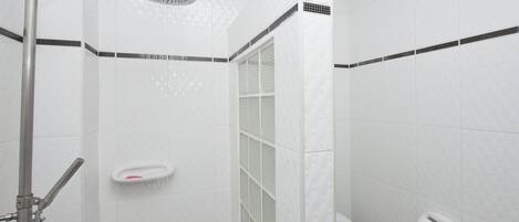 Ein Duschbereich mit Handbrause, einer gläsernen Duschkabine und einer Toilette mit Papierhandtuchspender.