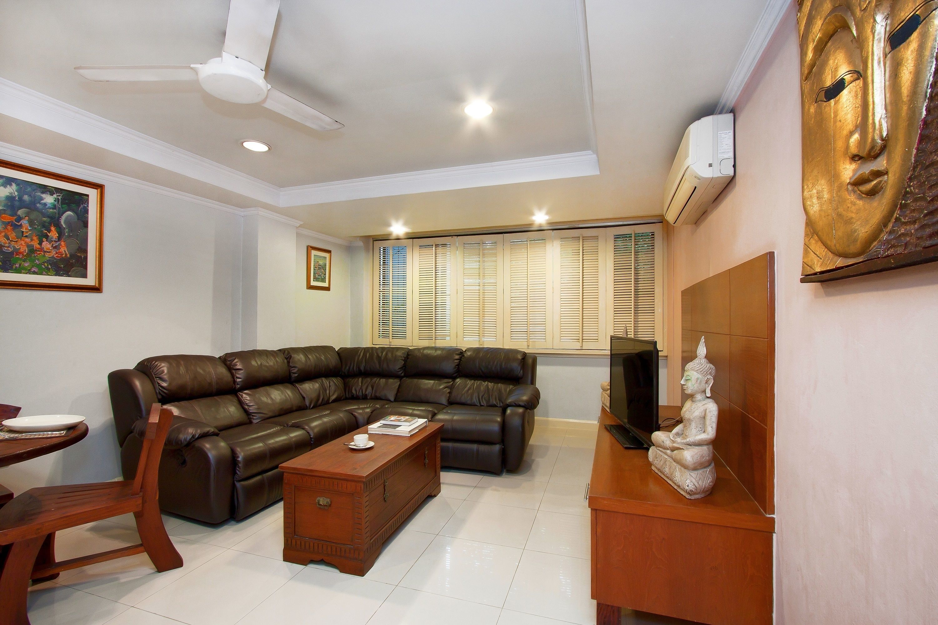 A living room with a leather sofa, wooden coffee table, and a statue on a wooden cabinet.