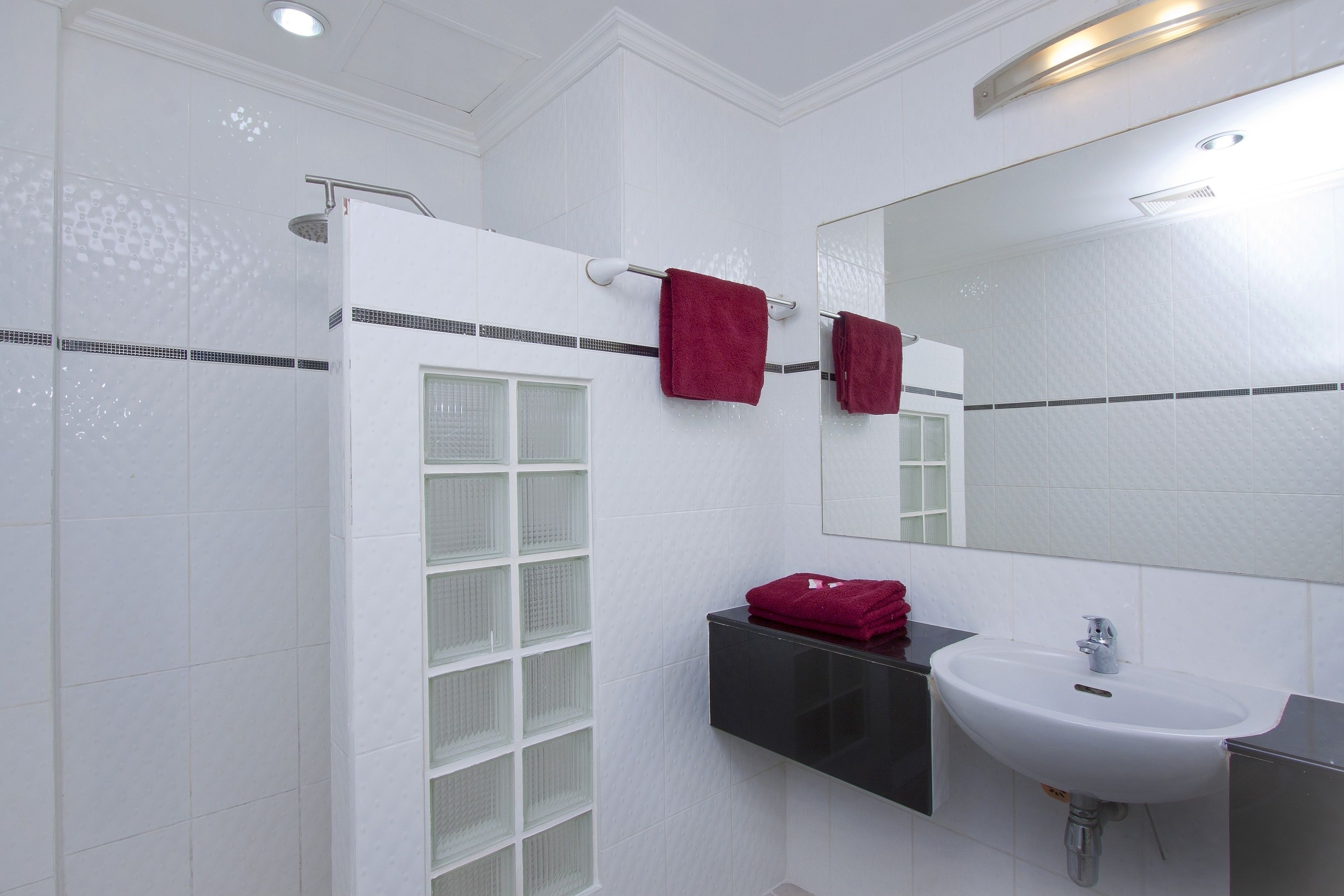 A modern bathroom with a white tiled shower, a black medicine cabinet, and a white sink.