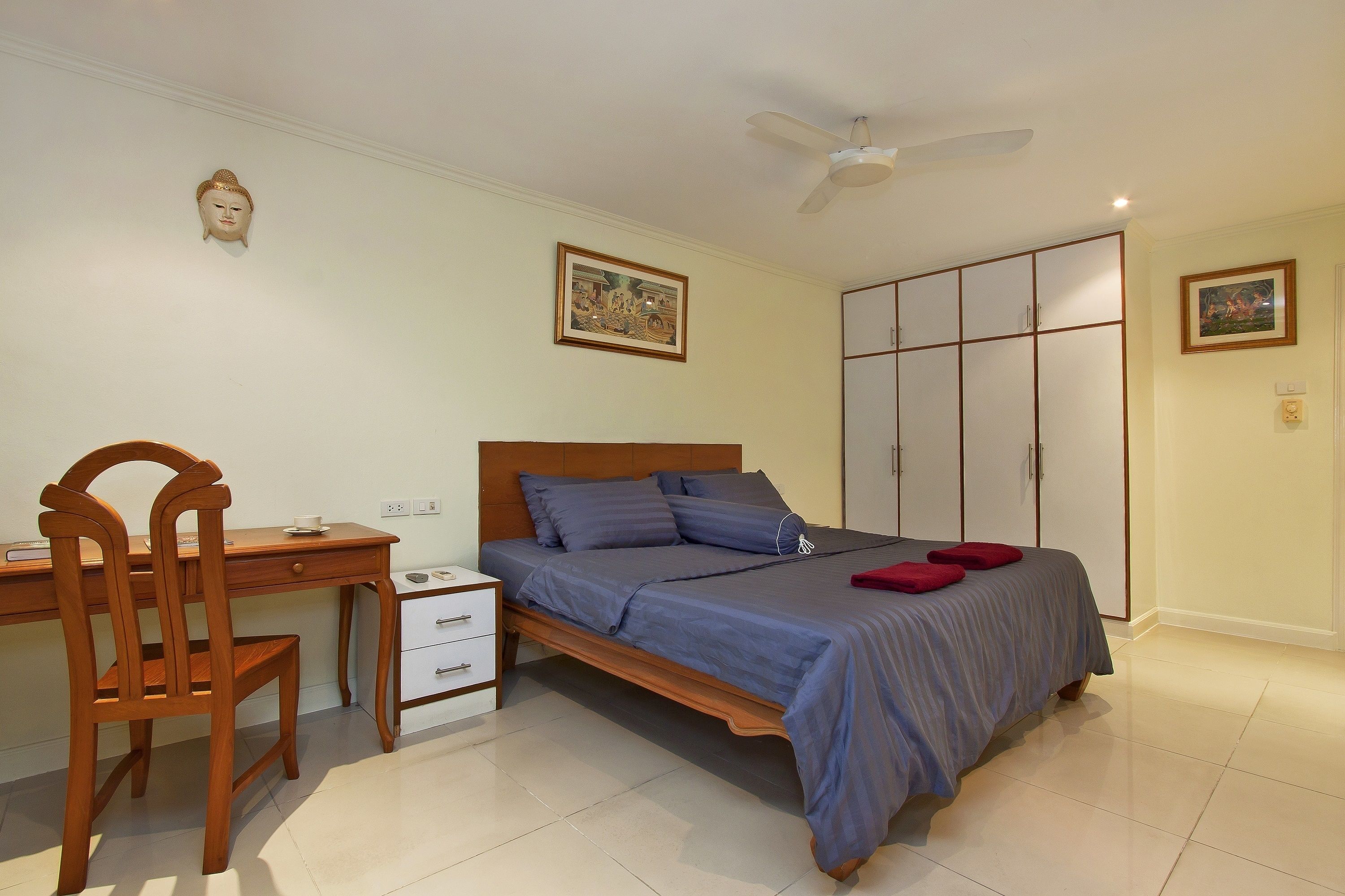 A bedroom with a bed, a desk, a chair, a wardrobe, and a ceiling fan.