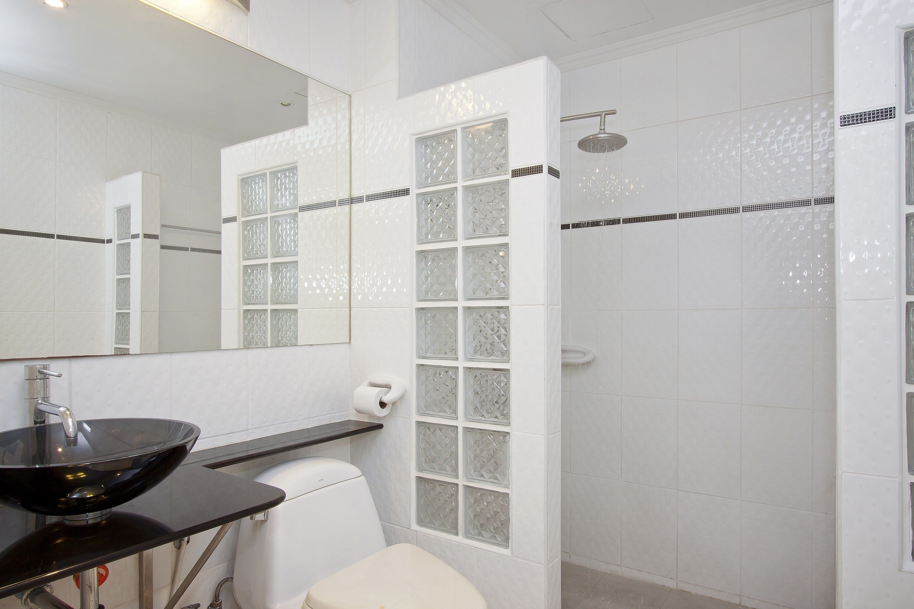 Un bany amb un lavabo negre, vàter blanc i cabina de dutxa de vidre.