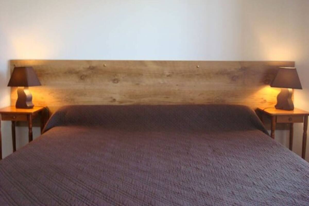 A bed with a wooden headboard, two bedside tables with lamps, and a plain wall.