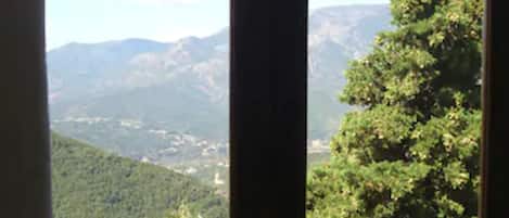 Une fenêtre donnant sur un paysage montagneux et une végétation luxuriante.