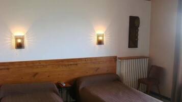A room with two single beds, a wooden headboard, a radiator, a wall-mounted light fixture, and a chair.