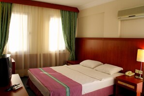Et hotelværelse med en seng, et natbord med lampe, telefon og et fjernsyn på et skrivebord.