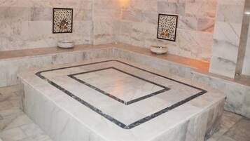 A marble-tiled bathroom with a central square sink, two wall-mounted towel racks, and a small decorative bowl on the countertop.
